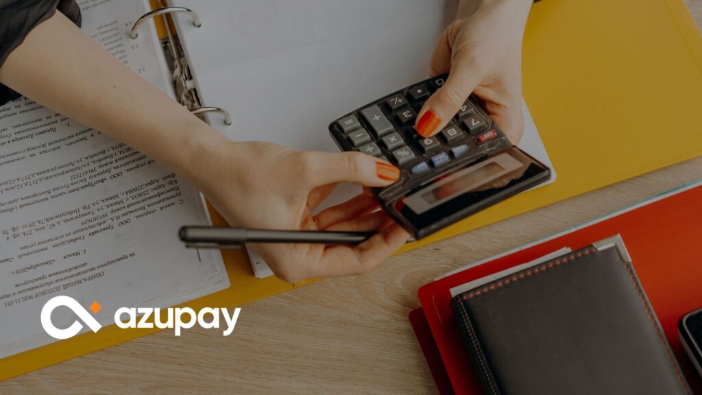 Hands holding a calculator and pen over financial documents, with binders on a desk with Azupay logo