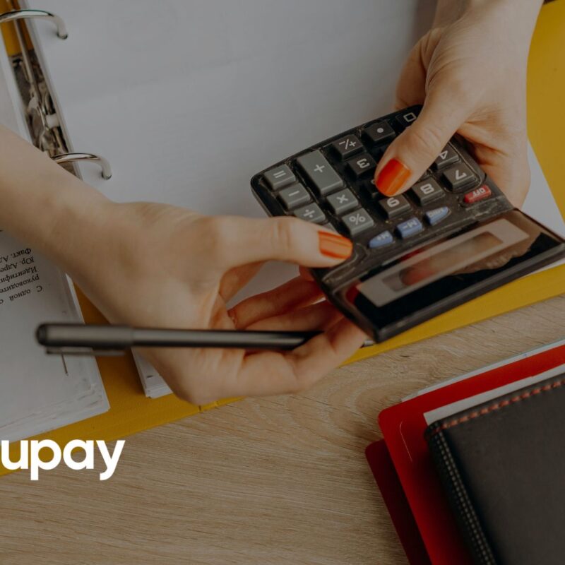 Hands holding a calculator and pen over financial documents, with binders on a desk with Azupay logo
