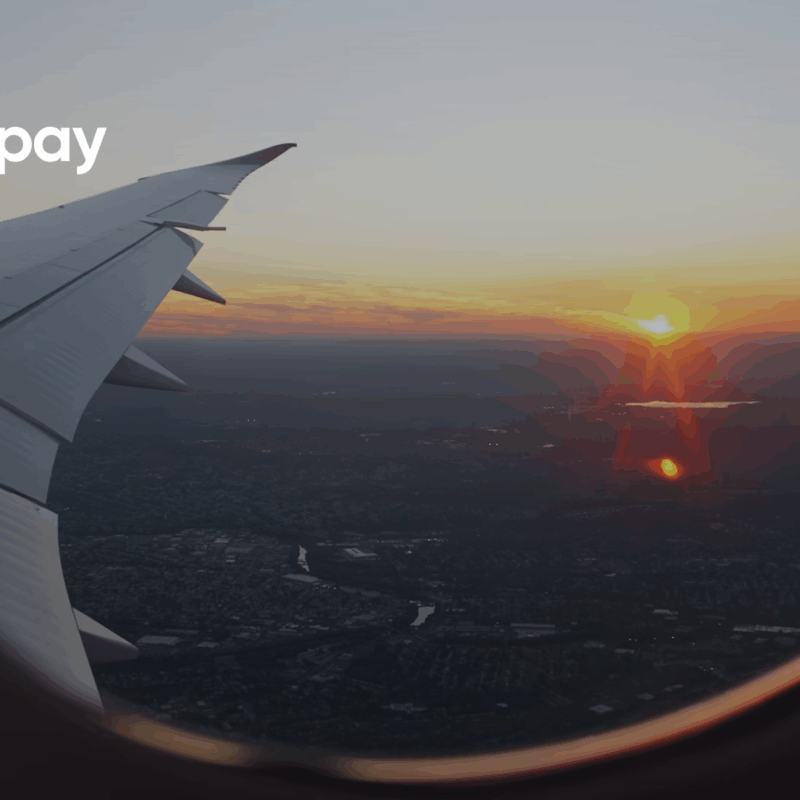 View from an airplane window at sunset showing the wing and landscape below, with Azupay’s logo on the top left corner.